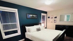 Un dormitorio con una cama, un aparador, una ventana con persianas y un cuadro colgado en la pared.