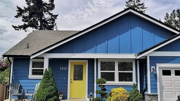 Una casa azul con una puerta amarilla, con el número 1110 y un garaje.