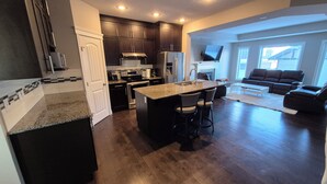 A modern kitchen with dark wood cabinets, stainless steel appliances, and a central island with bar stools. - Sean Comfy Home Modern Escape in Edmonton – Near Northgate  (Edmonton)