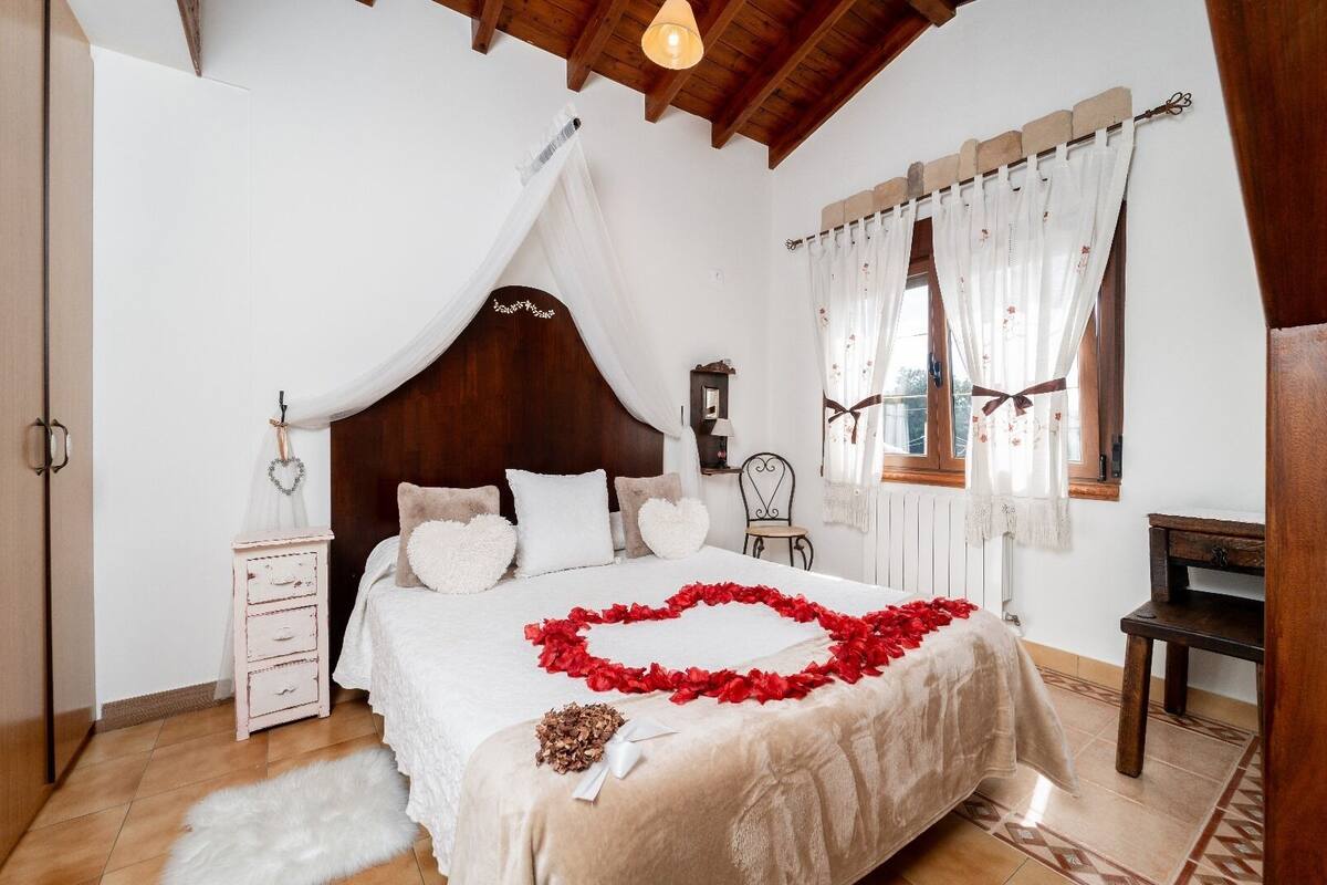 A bedroom with a canopy bed, a wooden dresser, a chair, and a window with curtains.