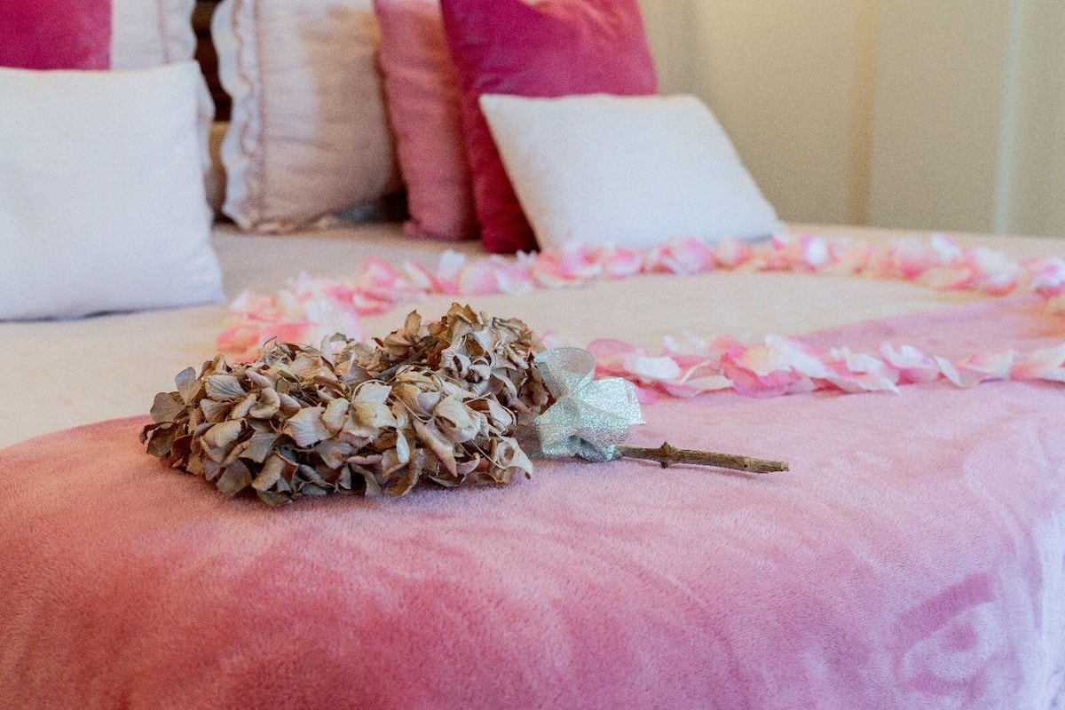 A bed with a pink blanket, a pine cone, and a decorative branch.