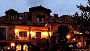 Un edificio grande de varios pisos con un balcón destacado y un muro de piedra al frente.