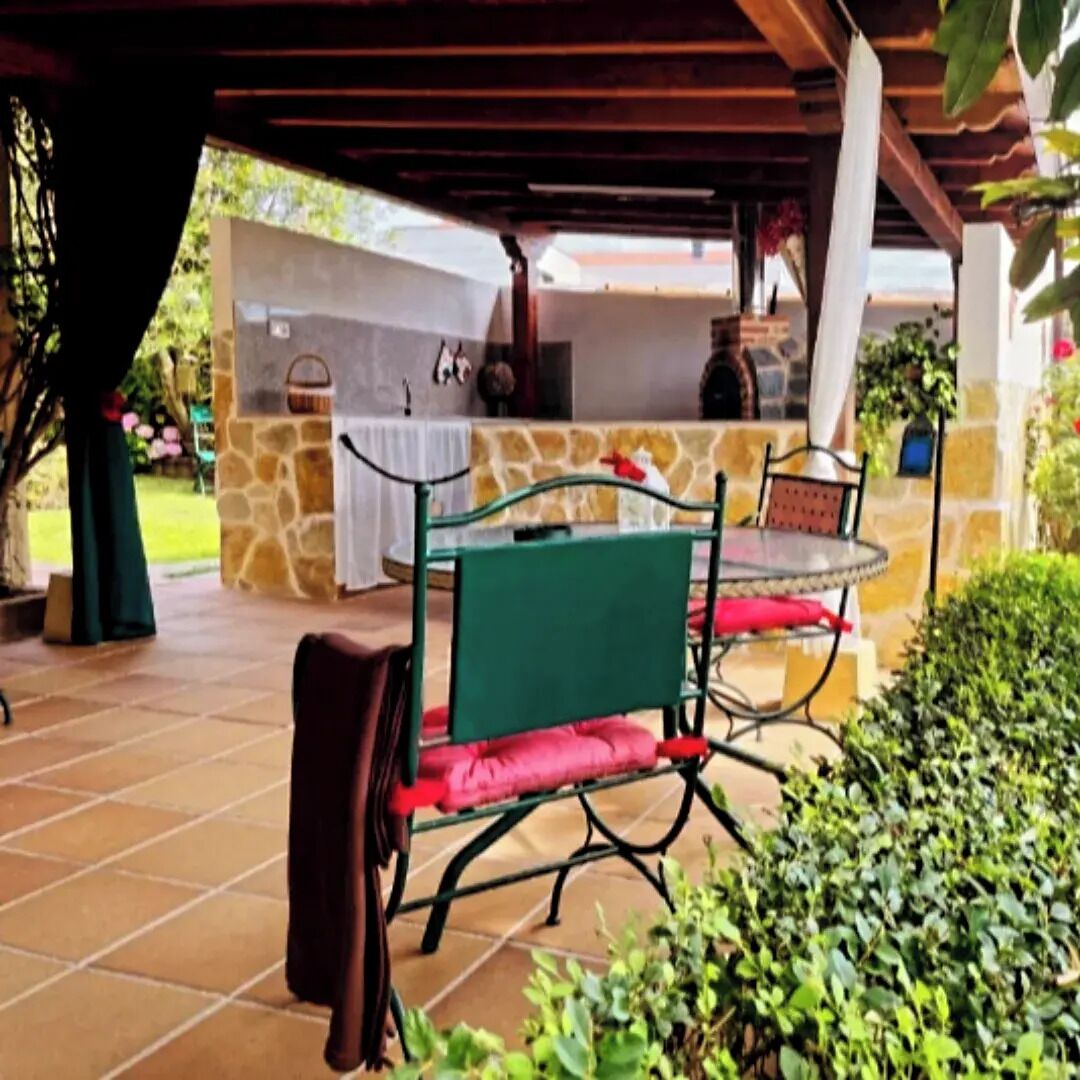 Une terrasse extérieure avec un mur en pierre, une table en verre et des chaises dotées de coussins rouges.