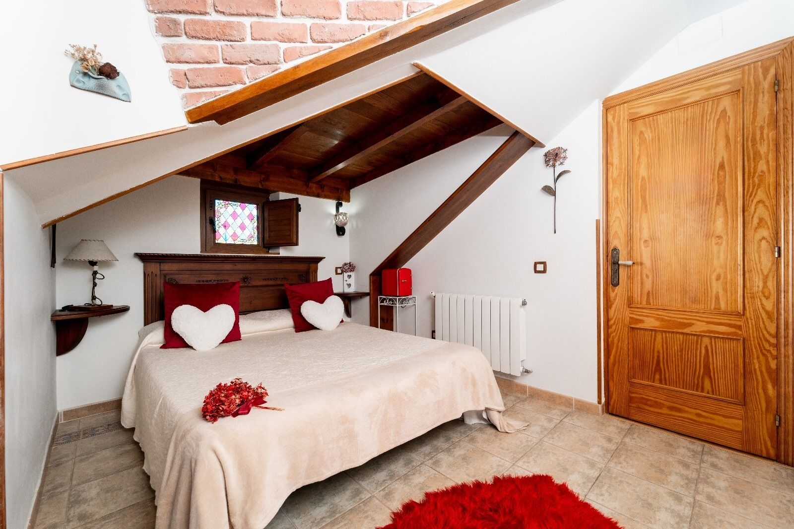 Een slaapkamer met een schuine kap, een houten bedframe, een radiator en een houten deur.