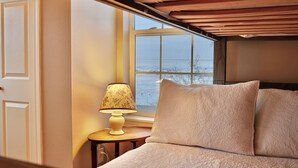 A bedroom with a bed, a lamp, and a window with a view of the outdoors.