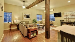 A spacious living room with a wooden ceiling, a large window, a television, and a dining area with a table and chairs.