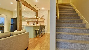 A modern kitchen with a central island, wooden beams, and a staircase with carpeted steps.