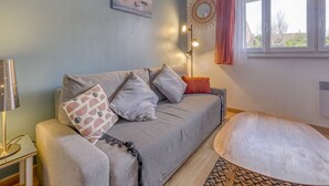 Ein Wohnzimmer mit grauem Sofa, gemusterten Kissen, einem runden Couchtisch, einer Stehlampe und einem Bild an der Wand.