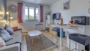 Ein kompakter Wohnbereich mit Sofa, einer kleinen Essecke mit Barhocker, Fernseher und Mini-Backofen.