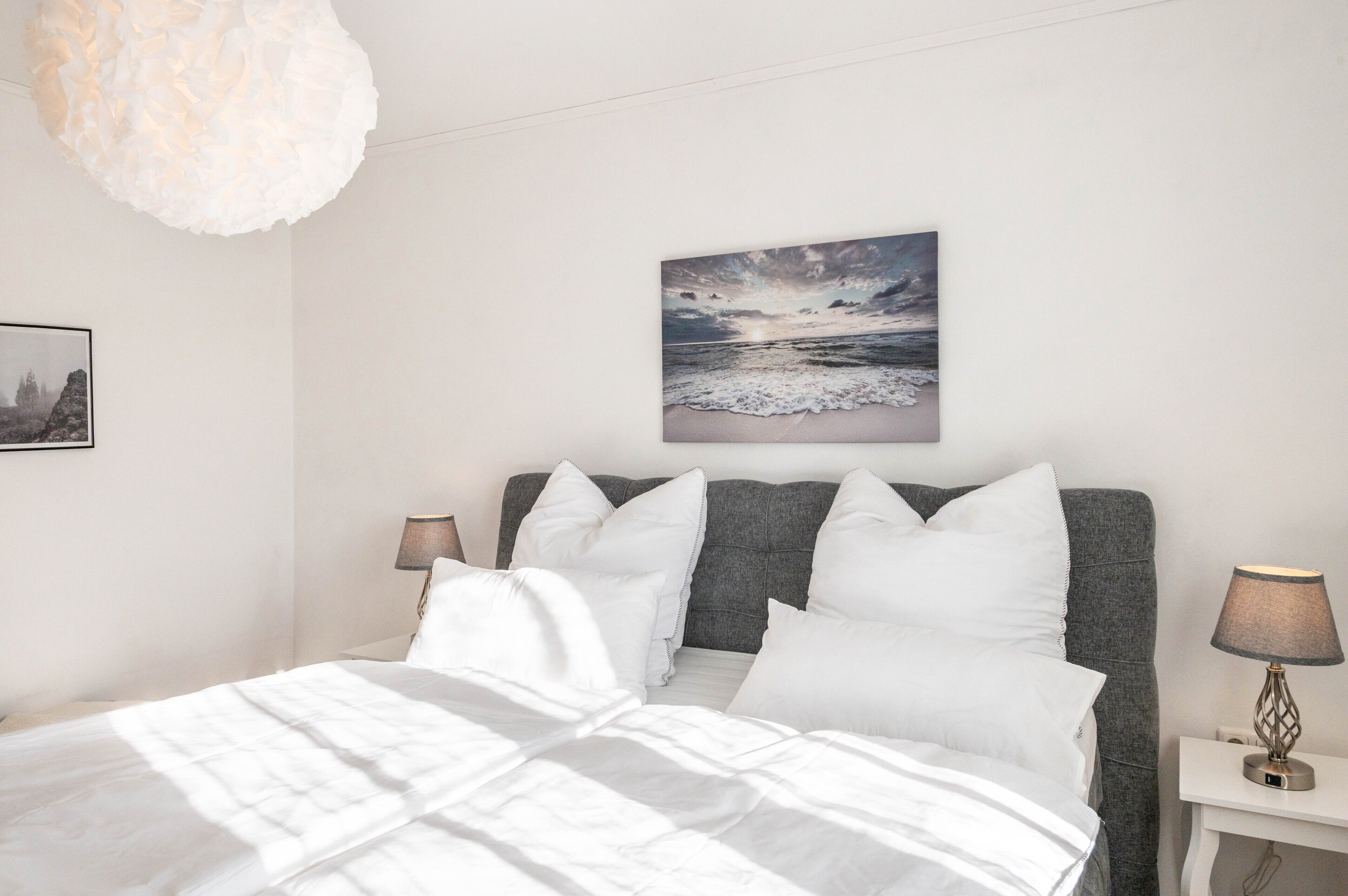 A bed with white bedding, a grey headboard, and a wall-mounted picture of a beach scene.