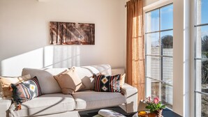 Ein Wohnzimmer mit einer Couch, Kissen, einem Couchtisch, einer Zeitschrift und einem Fenster mit Vorhängen.