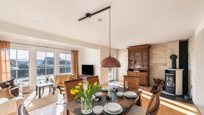 Ein geräumiges Wohnzimmer mit Essbereich, großen Fenstern, einem Kamin und einem Fernseher.