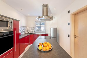 A modern kitchen with red cabinets, stainless steel appliances, and a central island with fruit. - Holiday Home 'Casa Meeresbrise am Vogelpark Marlow' with Terrace, Hot Tub & Garden (Marlow)