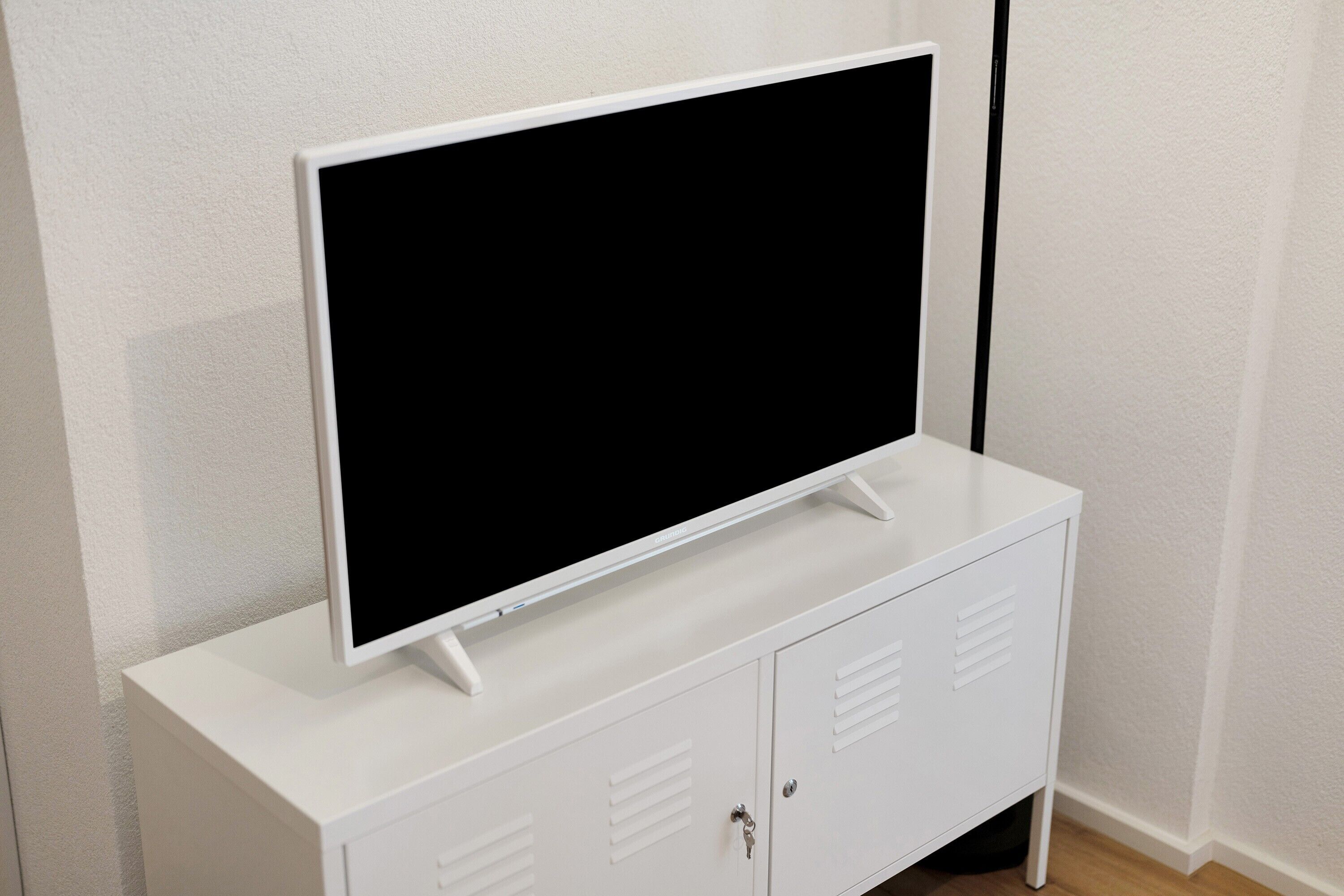 En vit TV-apparat står på ett vitt skåp med två luckor och ventilationsöppningar.