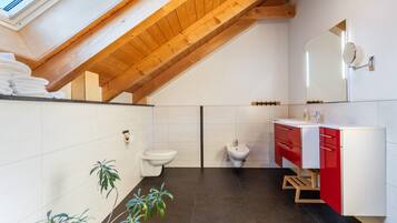 Een moderne badkamer met dakraam, witte tegels, een wastafel in rood en wit, een douchetoilet en twee toiletten.
