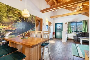 A room with a wooden dining table, chairs, a sofa, and a green curtain-covered window. - Apartment 'Blockhaus' with Mountain View, Shared Garden and Wi-Fi (Augustusburg-Erdmannsdorf)