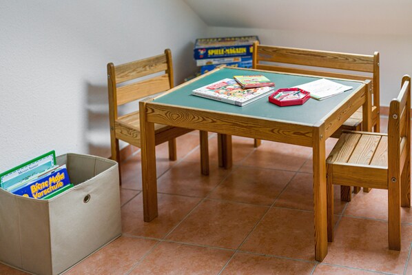 A wooden table with chairs, a green tablecloth, and a storage box with books.