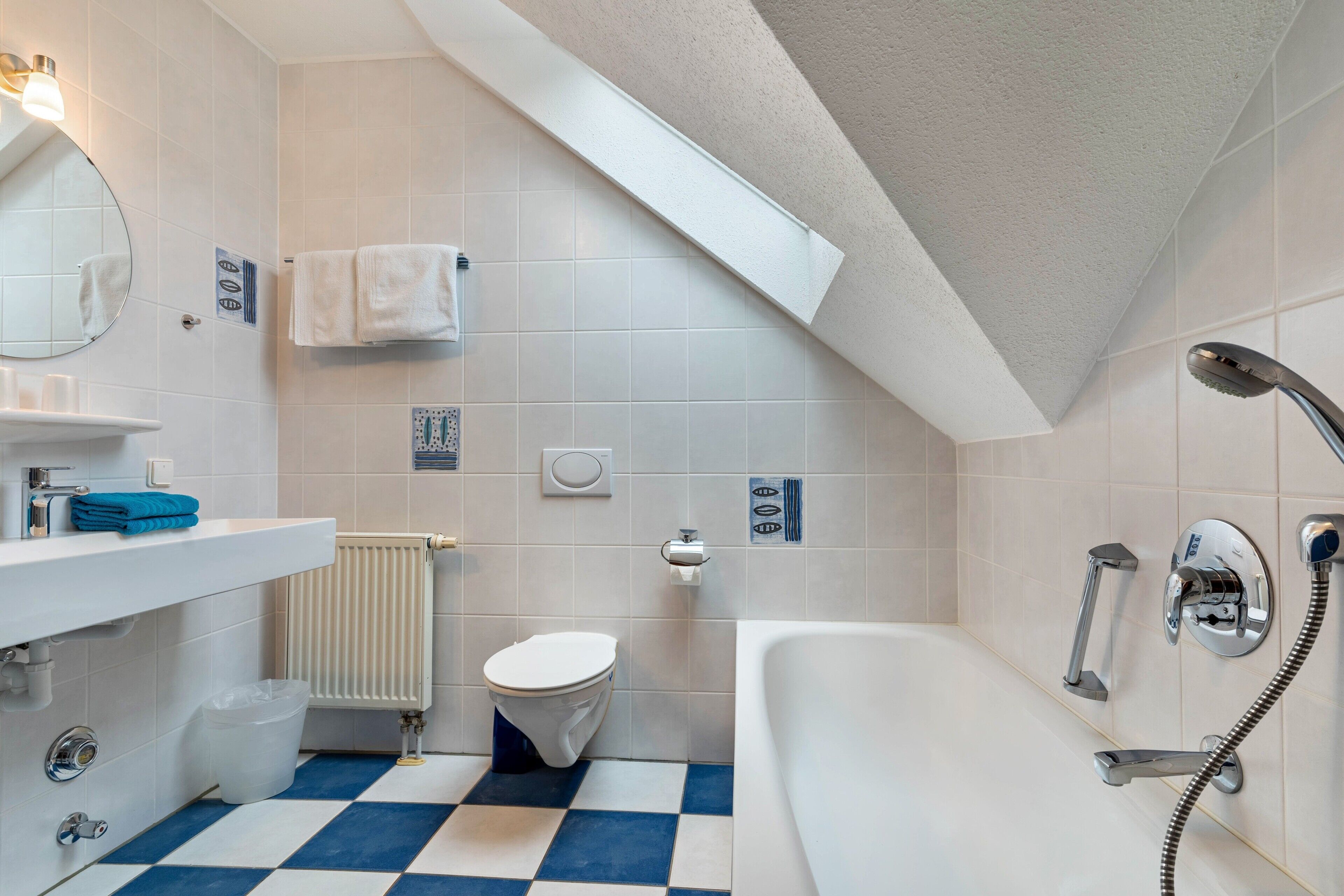 A bathroom with a checkered floor, a toilet, a sink with a mirror, and a bathtub with a showerhead.