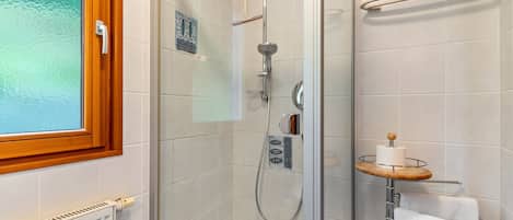 A shower with a glass door, a towel rack, and a toilet paper holder.