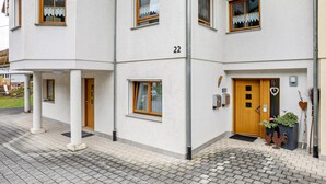 A multi-story building with a white facade, numbered 22, featuring a wooden door, windows with curtains, and a small garden area with decorative elements. - Holiday Apartment 'Sum' with Mountain View, Shared Garden, and Wi-Fi (Oberwolfach)