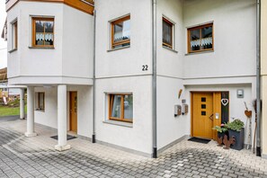 Un edificio de varios pisos con fachada blanca, número 22, que presenta una puerta de madera, ventanas con cortinas y un pequeño jardín con elementos decorativos.