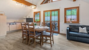 A modern kitchen with wooden cabinets, a dining table with chairs, a black leather sofa, and large windows with curtains. - Holiday Apartment 'Sum' with Mountain View, Shared Garden, and Wi-Fi (Oberwolfach)