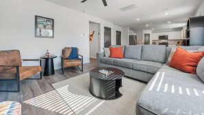 A modern living room with a grey sofa, a coffee table, and a ceiling fan. - Charming 4-bedroom house with movie room, game room, outdoor patio + fire pit  (Bryan)