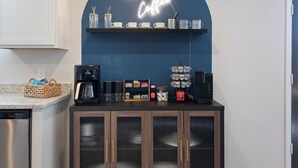 A kitchen with a coffee station, including a coffee maker, cups, and a neon sign that reads "BUT FIRST Coffee". - Charming 4-bedroom house with movie room, game room, outdoor patio + fire pit  (Bryan)