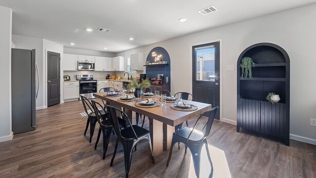 A modern kitchen with white cabinets, a wooden dining table set for four, and a black archway with a plant shelf. - Charming 4-bedroom house with movie room, game room, outdoor patio + fire pit  (Bryan)