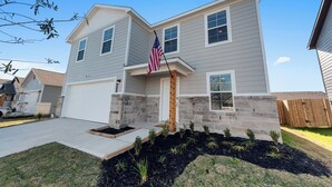 A two-story house with a front porch, a garage, and a small garden area with young plants. - Charming 4-bedroom house with movie room, game room, outdoor patio + fire pit  (Bryan)