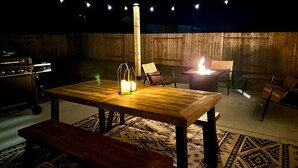 An outdoor patio with a wooden table, chairs, a bench, and a fire pit. - Charming 4-bedroom house with movie room, game room, outdoor patio + fire pit  (Bryan)