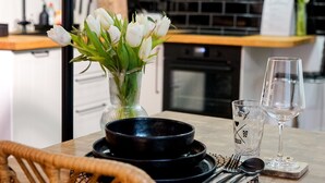 Una mesa de comedor con un jarrón de flores blancas, un bol negro y dos copas de vino.