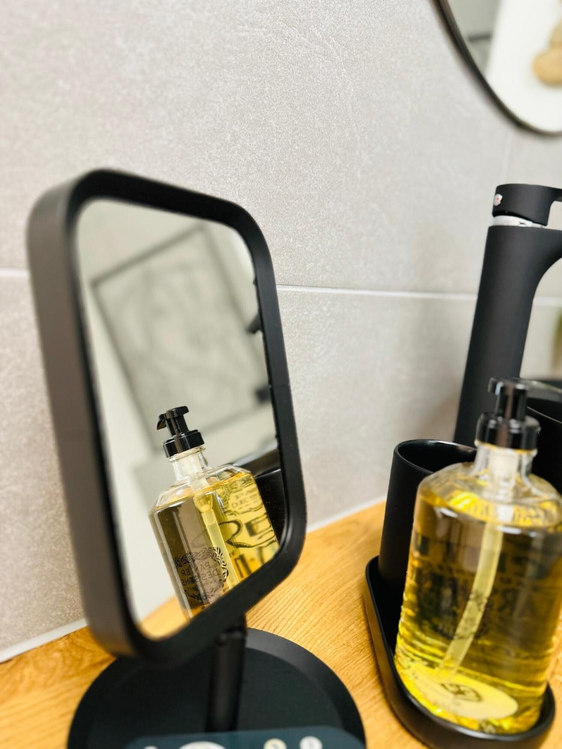 Et badeværelsesspejl med sort ramme, en sæbeflaske og en sort sæbedispenser.