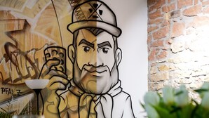 Una habitación con un mural, una pared de piedra, un sofá, una mesa con vasos y un florero.