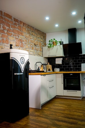 A kitchen with a stone wall, a black refrigerator, a wooden countertop, white cabinets, a black tiled backsplash, and a black oven. - Apartment 'Heimat - Bad Dürkheim' with Wi-Fi (Bad Dürkheim)