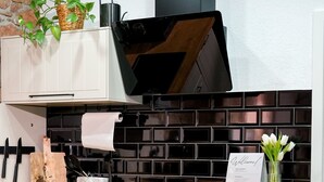 Una cocina con armarios blancos, un salpicadero de baldosas negras, encimera de madera y un lavamanos de acero inoxidable, además de una silla negra.
