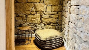 Una habitación con paredes de piedra y techo de madera, una mesa redonda y un otomano tejido.