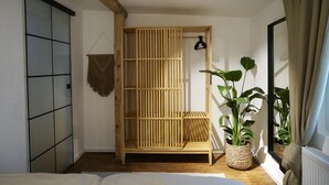 Une chambre avec un cadre de lit en bois, une plante suspendue, un panier tressé et une fenêtre avec des rideaux.