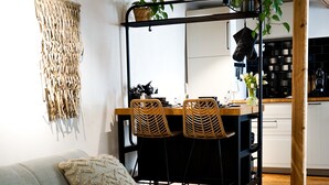 Un salon moderne comprenant un canapé, une table à manger avec des chaises, un coin cuisine et une plante suspendue.