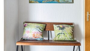 Een houten bank met twee kussens, waarvan één een bloemenprint en tekst heeft, en de ander een vogelkooi-design en tekst.