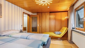 Una habitación con dos camas, techo de madera, una silla amarilla y una ventana.