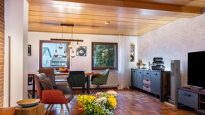 Una sala de estar moderna con comedor, techo de madera, paredes de ladrillo y un ventanal grande.