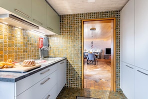 Une cuisine avec un mur recouvert de carreaux, un plan de travail sur lequel se trouvent des aliments et une porte donnant sur un coin repas.