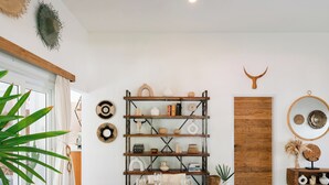 Een eetgedeelte met een ronde houten tafel, rieten stoelen en een boekenkast met decoratieve objecten.
