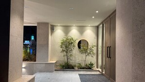 Una entrada de edificio moderno con suelo de baldosas, un pequeño jardín con plantas y una puerta con manija.
