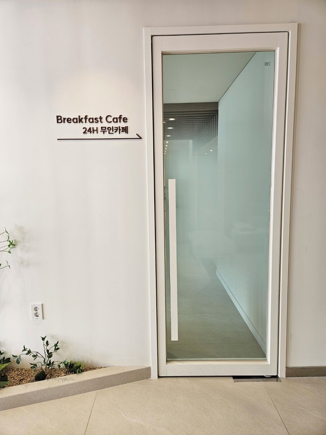 A modern entrance to a building with a sign indicating a 24-hour breakfast cafe.