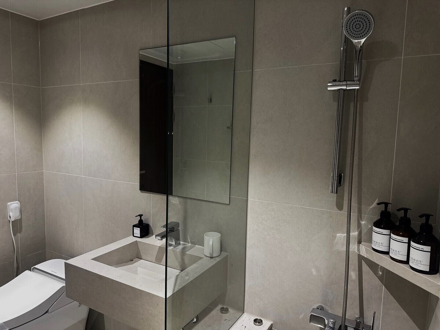 A modern bathroom with a large mirror, a shower, and a sink with toiletries.