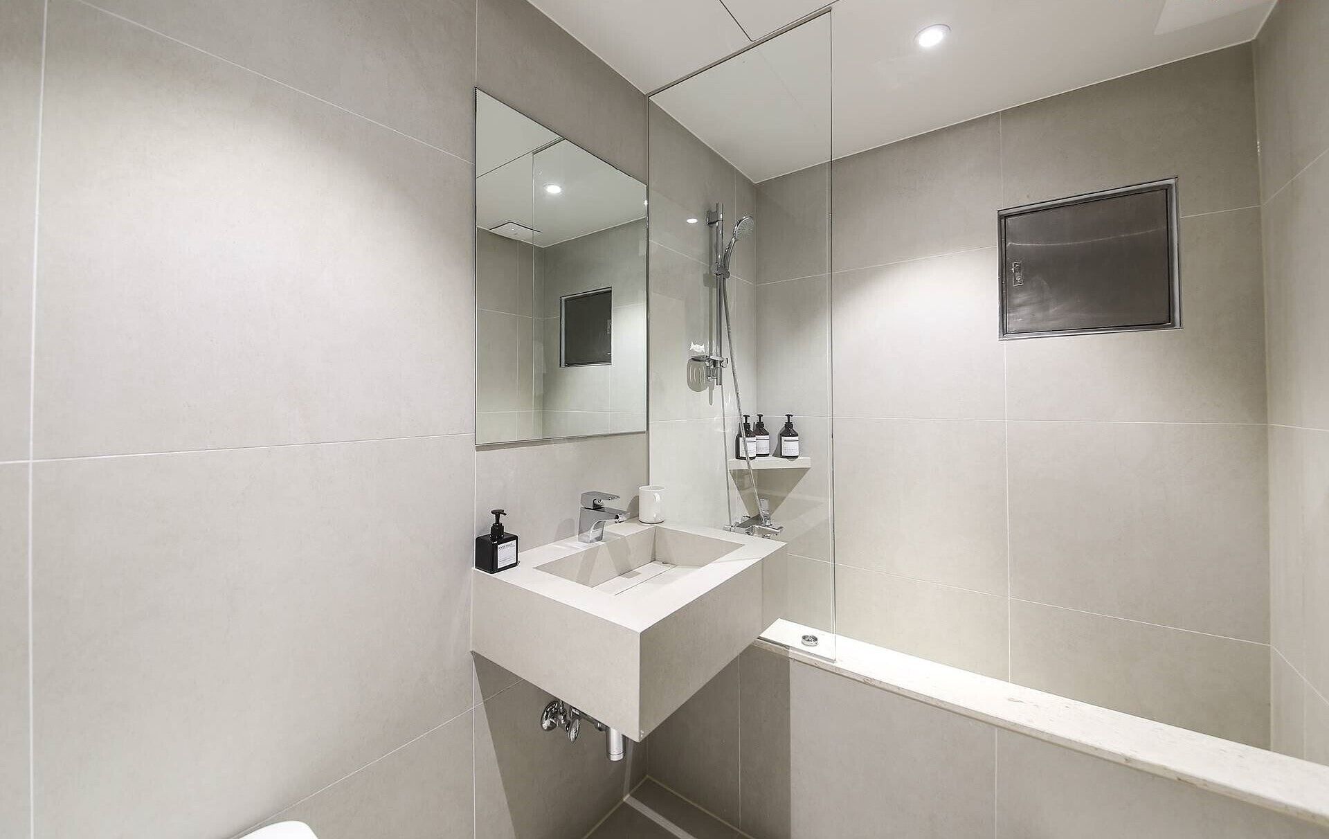 A modern bathroom with a large mirror, a sink, a shower, and a toilet.