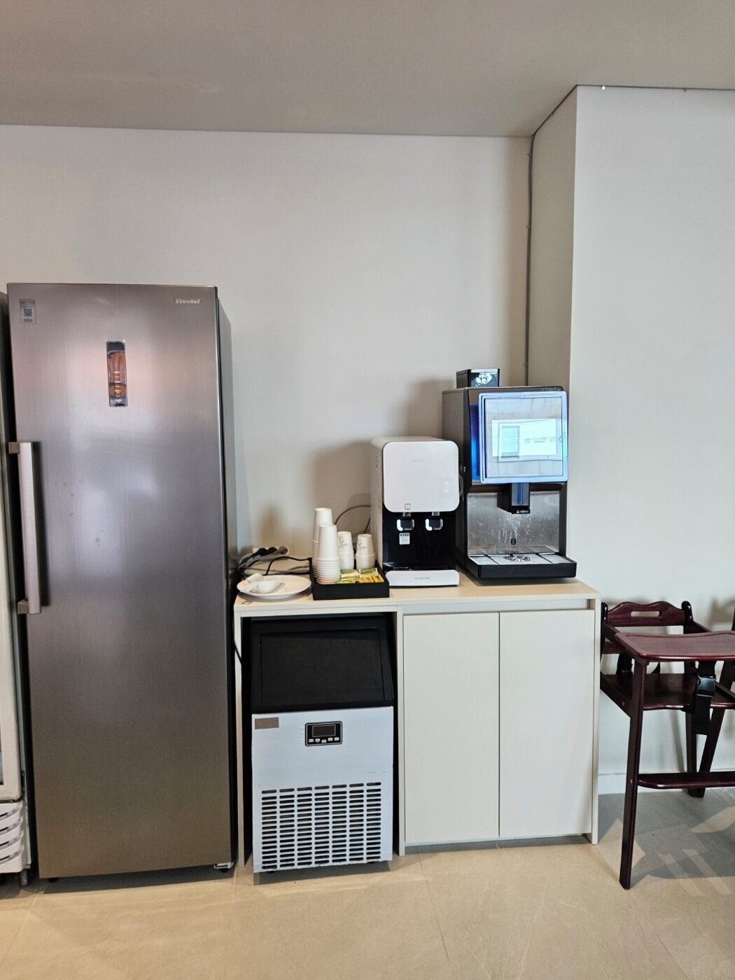 Uma cozinha compacta com geladeira de aço inoxidável, máquina de café e um pequeno refrigerador embaixo.