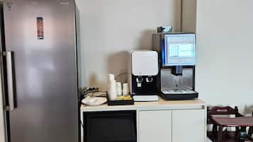 Uma cozinha compacta com geladeira de aço inoxidável, máquina de café e um pequeno refrigerador embaixo.